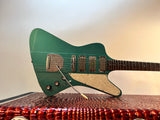 A teal green electric guitar with a cream pickguard and chrome hardware, resting on a textured red and black speaker cabinet against a plain light background.
